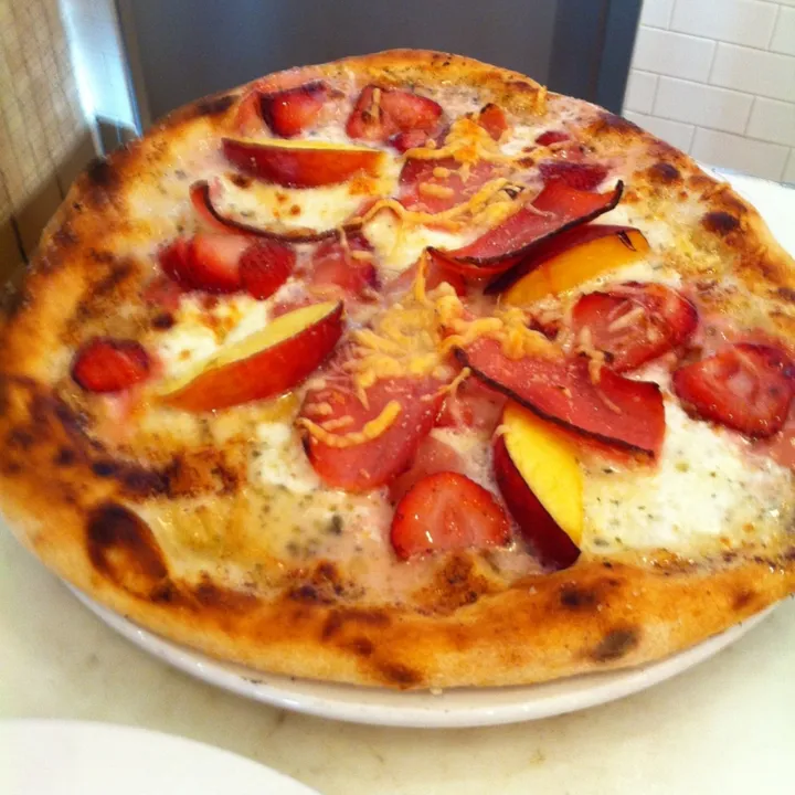 Wood-fired pizza with sliced tomato and nectarine on a white plate