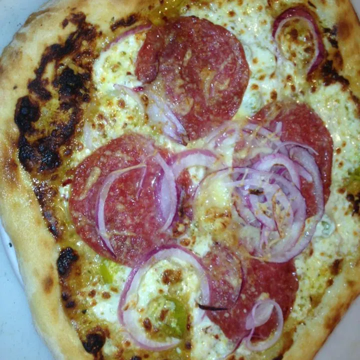 Pizza topped with salami, red onion and green olives, charred crust