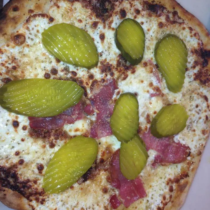Pizza topped with sliced pickles and cured meat