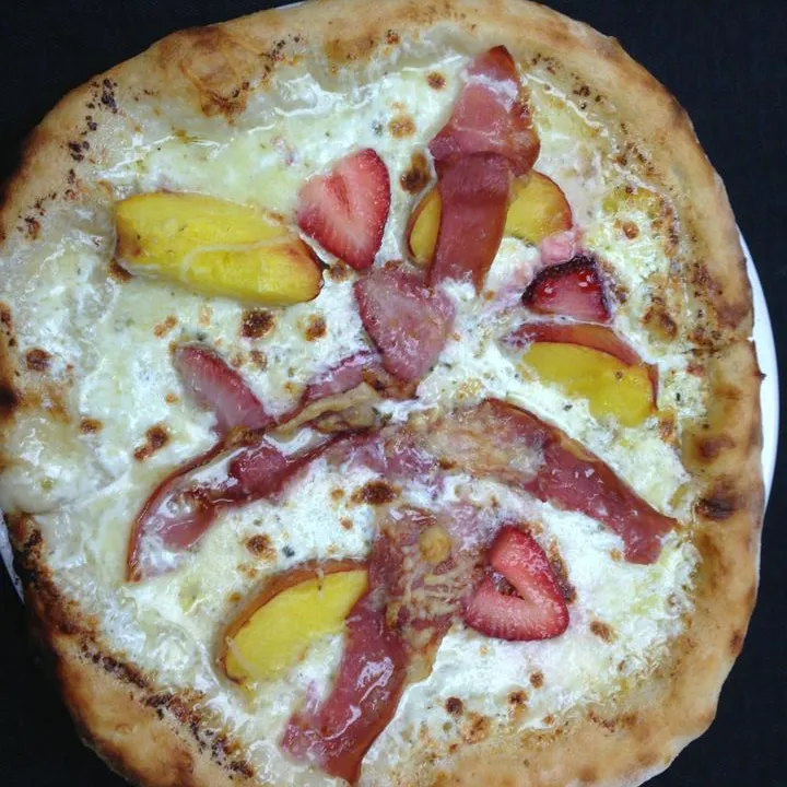 White pizza with prosciutto, strawberry and peach slices on a dark table