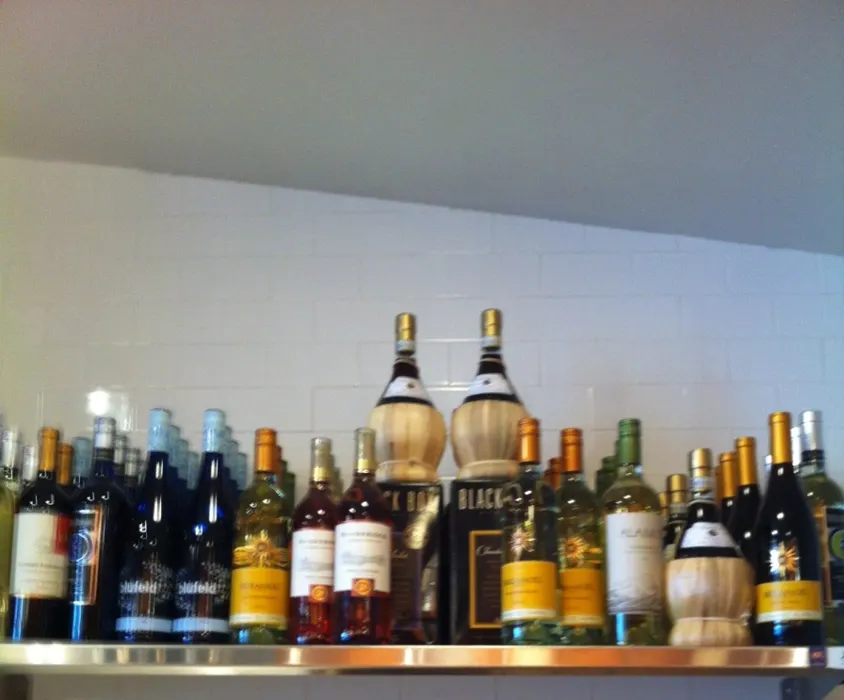 Shelf of red and white wine bottles above white tile at Pompeii Pizzeria